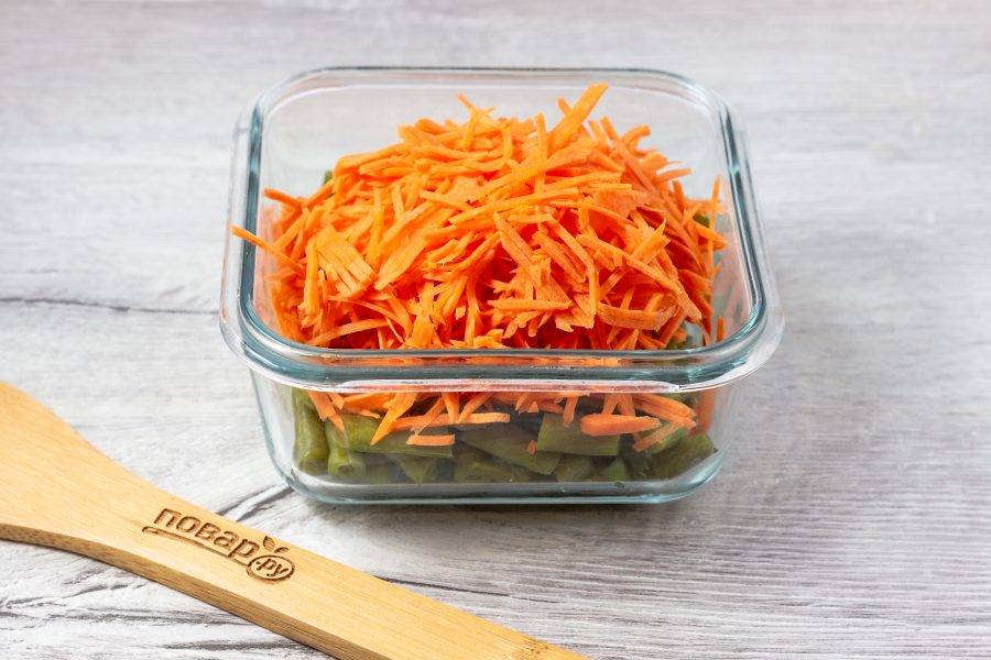 В салатник выложите подготовленную фасоль, морковь почистите и натрите на терке для корейской моркови. Добавьте к фасоли.