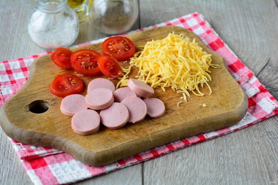 Также для начинки нарежьте колечками сосиски, помидоры и натрите сыр на терке.