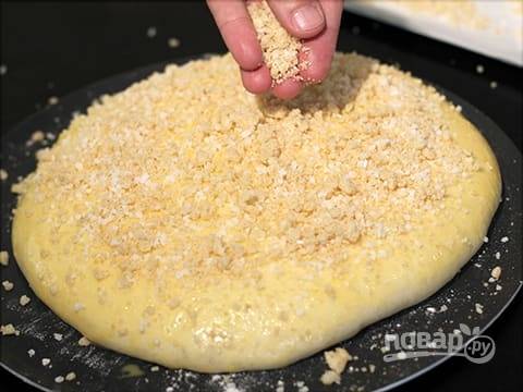 Дрожжевое тесто раскатайте пластом толщиной в 3 см, смажьте взбитым желтком, и посыпьте сверху крошкой.