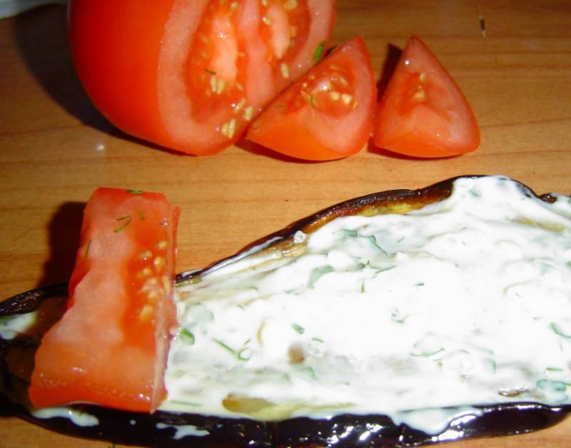 3. Промазываю соусом баклажан изнутри и кладу дольку помидора, после чего закручиваю полоску в рулет и выкладываю в форму для запекания.