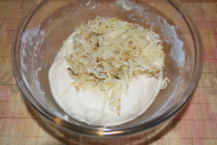 На растительном масле обжарьте нарезанную капусту. Тушите, добавив специй и соли. Капуста должна быть мягкой, нежной, почти готовой. Остудите ее и добавьте в подошедшее тесто. Снова вымесите. Затяните пленкой и дайте подняться около 30 минут.