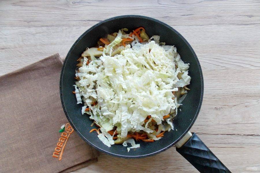Пекинскую капусту нарежьте соломкой и добавьте в сковороду с луком, морковью и баклажаном. Добавьте измельченный чеснок.