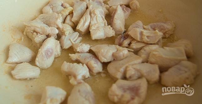В сковороду влейте немного растительного масла, поставьте ее на плиту. Когда масло разогреется, обжарьте на нем кусочки курицы на среднем огне до золотистого оттенка. 