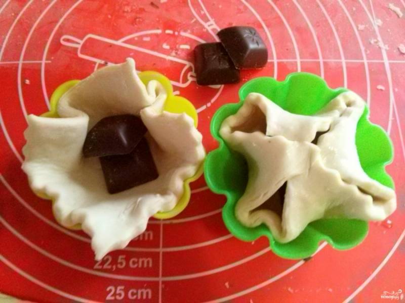 Разложите  заготовки из теста в формы для кексов, внутрь каждой положите по два квадратика шоколада.