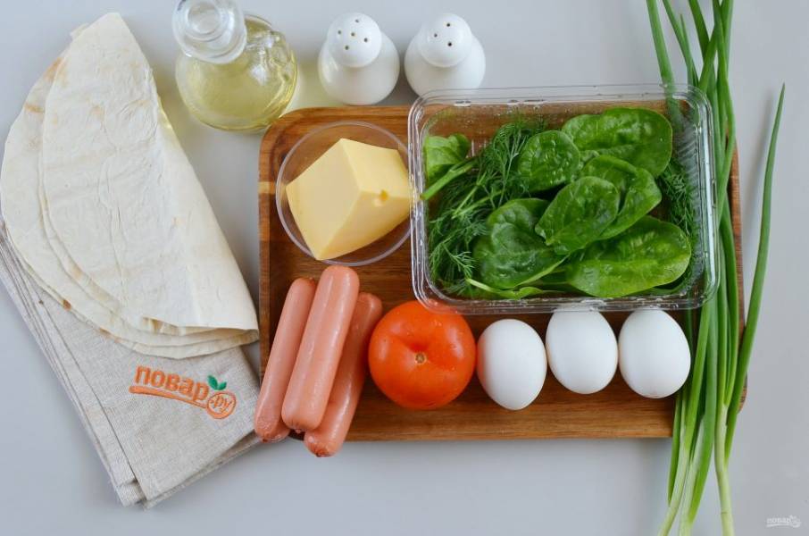 Подготовьте ингредиенты. Вымойте зелень, помидор, разверните сосиски. Подберите сковороду диаметром равным лавашу, или подгоните размер лаваша под размер сковороды.