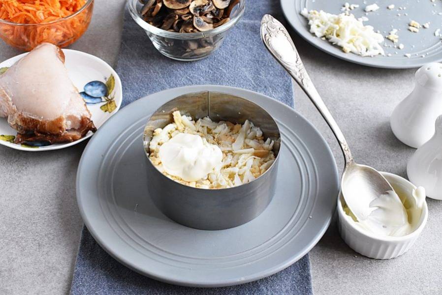 Натрите крутые яйца на крупной терке и выложите первым слоем в салатник или кольцо. Слегка присолите и смажьте тонким слоем майонеза.