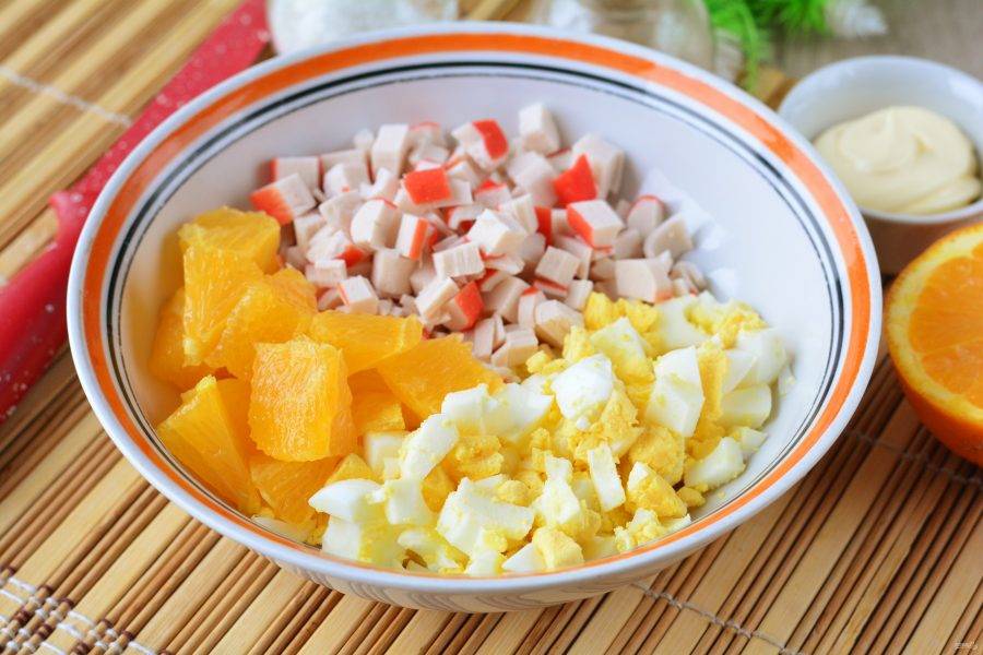 В глубокую миску отправьте все нарезанные ингредиенты — яйца, апельсины и крабовые палочки.