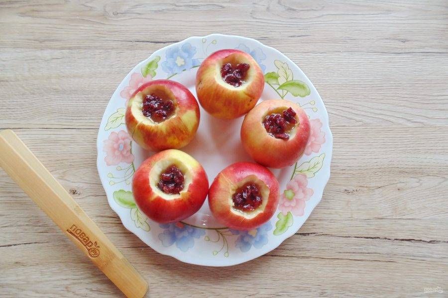 Вяленую клюкву ополосните и обдайте кипятком. Выложите по несколько ягод в каждое яблоко.