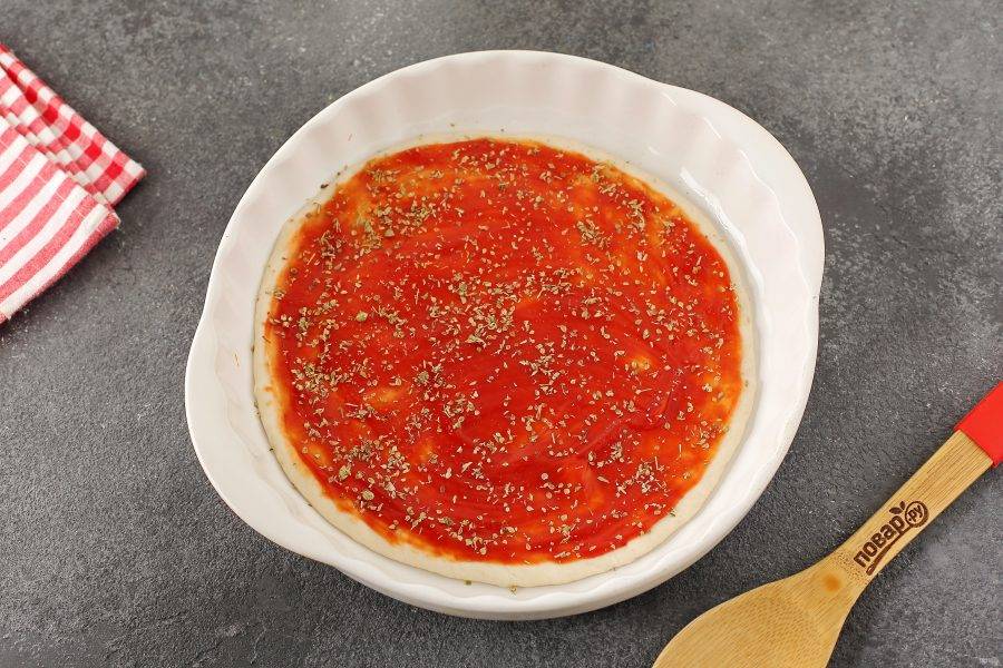 Затем смажьте тесто томатным соусом и посыпьте специями (орегано, базилик или прованские травы).