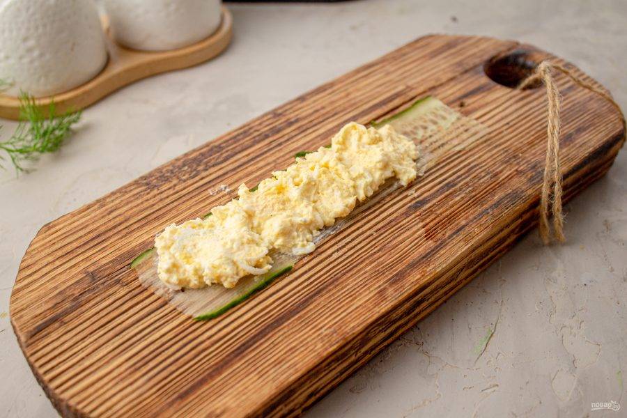 Выложите полоску огурца на поверхность, примерно  2/3 части смажьте начинкой из яиц и сыра.