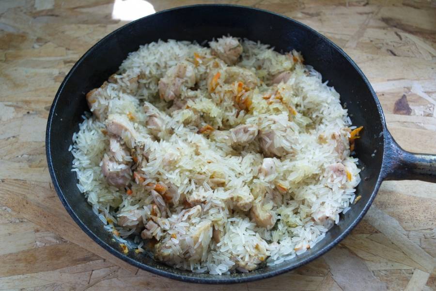 6. К мясу с овощами добавляем сухой сырой рис. Даем рису пропитаться маслом и соком курицы.
