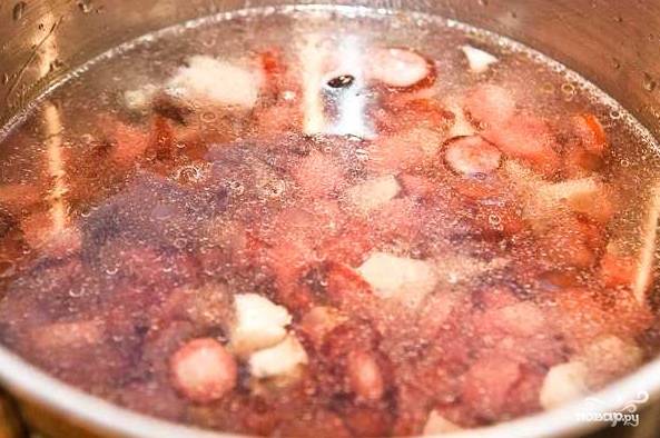 6. Выложите в кипящую воду колбаски и обжаренный с пастой лук. Добавьте по вкусу соль. 