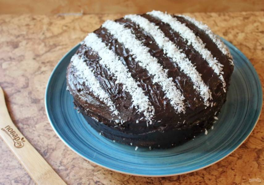 Покройте торт шоколадной глазурью. Вырежьте из бумаги полоски. Выложите их на торт. Открытые места торта посыпьте белой кокосовой стружкой. После бумагу снимите.