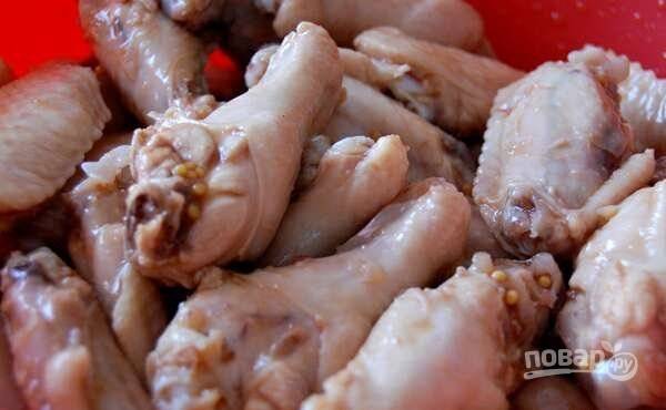 Курицу переложите в глубокую посуду. Влейте к ней уксус, перемолотый чеснок, соус, сахарную пудру и горчицу. Всё перемешайте. Оставьте крылышки мариноваться на 1-2 часа.