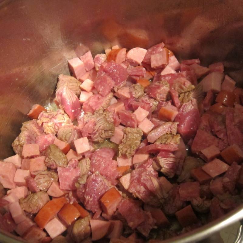 1. Все колбасные изделия нарежем кубиками, мясо тоже порежем кубиками и обжарим на сковороде. Поместим в кастрюлю вместе с остатками масла. 