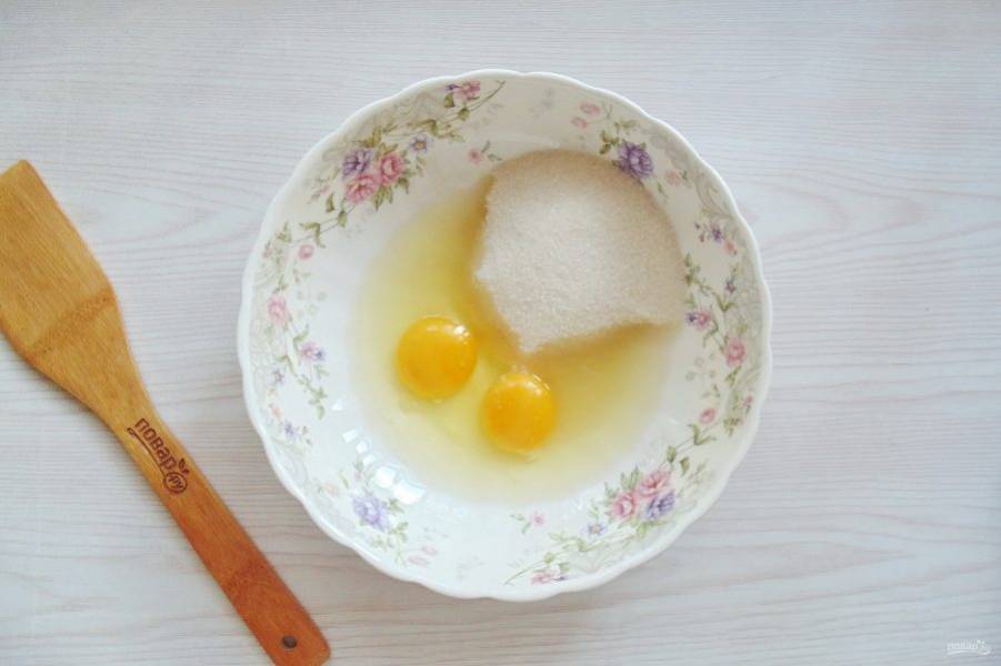 Приготовьте тесто для торта. В миску разбейте яйца и насыпьте сахар.