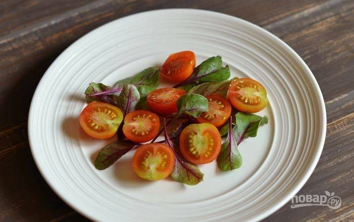 Листья любого зеленого салата на ваш вкус вымойте и обсушите. Затем выложите их на тарелку. После этого вымойте помидоры черри и разрежьте каждый томат на две части. Выложите помидоры к листьям салата. 