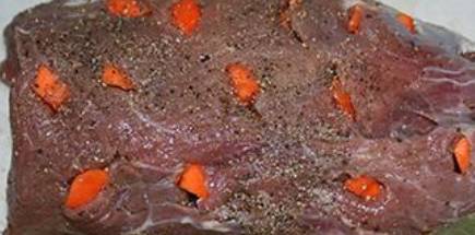 4. Теперь подготовим кусок говядины (удалим жир и пленочки, если есть), и делаем в нем надрезы по всей поверхности, куда помещаем чеснок и морковку. Натираем мясо солью и специями по вкусу.