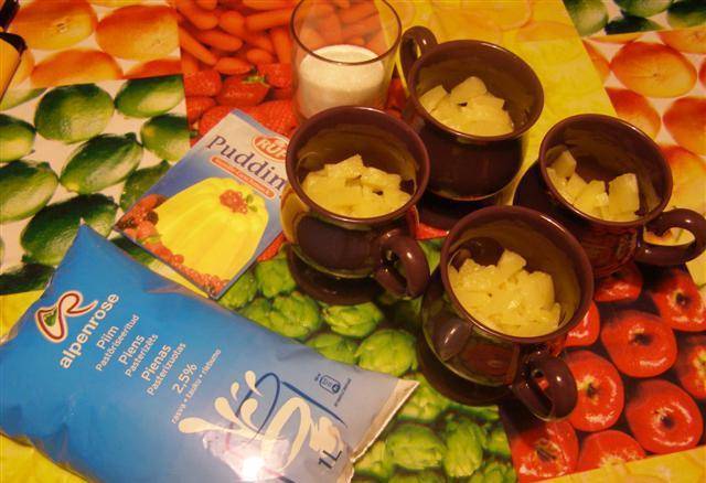 Подготовьте порционные чашечки для пудинга. Кусочками порежьте консервированные колечки ананасов. Наполните ими чашки на 1/3.
