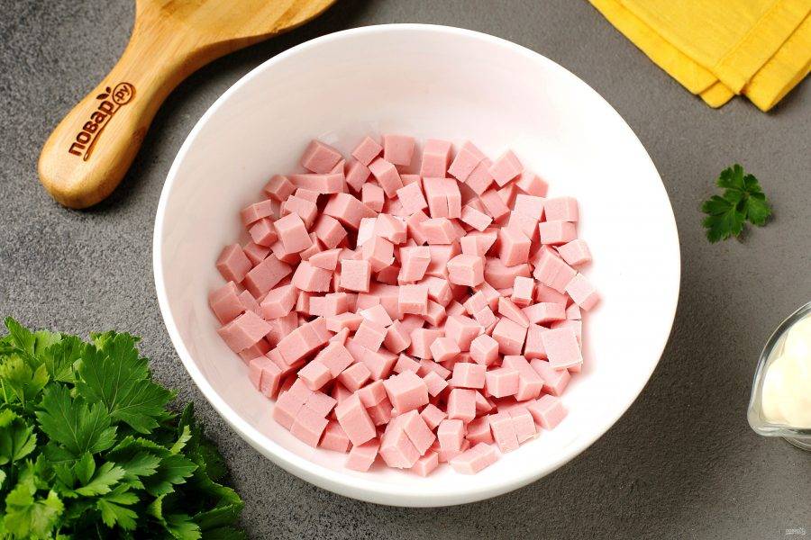 Колбасу нарежьте кубиками и переложите в салатник.