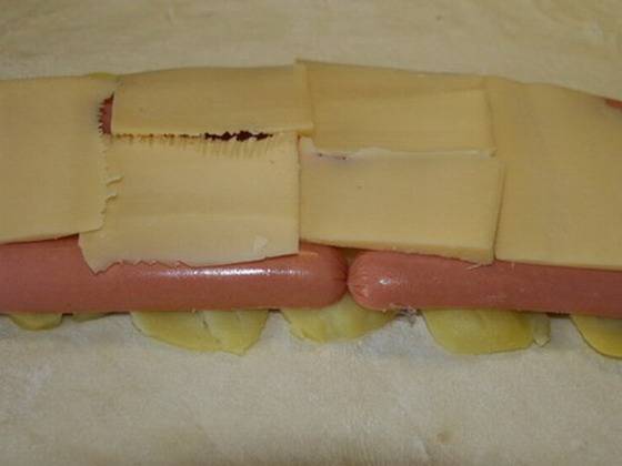 Нарезаем тонкими ломтиками сыр, укладываем на сосиски.