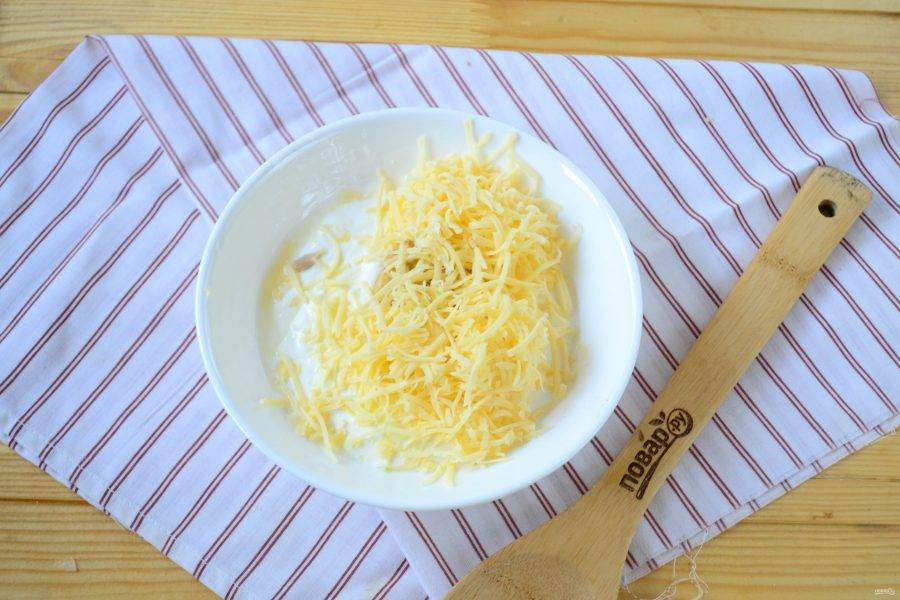 Теперь займемся соусом. Сыр натрите на мелкой терке. Смешайте сыр со сметаной, горчицей, лимонным соком, щепотками соли и перца. Туда же выдавите несколько зубчиков чеснока.