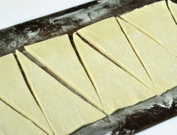 Размораживаем готовое слоеное тесто и слегка раскатываем. Нарезаем тесто на треугольники.