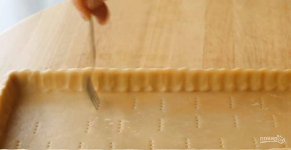 2. Тесто раскатайте в пласт толщиной 0,5 см. Выложите тесто в форму, сформировав бортики. Наколите тесто вилкой, выстелите на него пергамент и насыпьте груз. Отправьте в холодильник на 20 минут. 