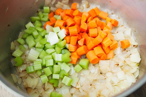 5. Добавьте на сковороду еще немного масла, отправьте туда сначала измельченный репчатый лук, а через пару минут — сельдерей и морковь. Также можно использовать сладкий перец. 