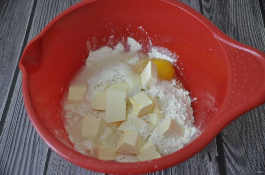 В миску для замешивания теста добавьте просеянную муку, разрыхлитель, соль, охлажденное масло, порезанное крупным  кубиком, яйцо и 5 столовых ложек ледяной воды.