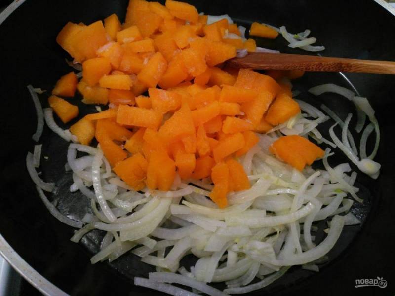 Пока выпекается основа рулета, приготовьте начинку: мелко порежьте овощи (репчатый лук, тыкву и чеснок). Поместите лук на разогретую сковороду, смазанную подсолнечным маслом. Пассеруйте лук в течение 1-2 минут, добавьте тыкву.