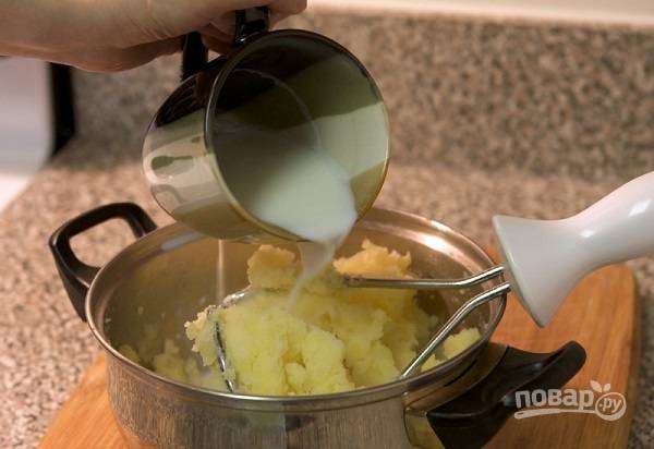 4. Влейте горячее молоко, продолжая мять пюре. Если вы любите более жидкую консистенцию, добавьте еще немного воды, в которой варили картофель. 