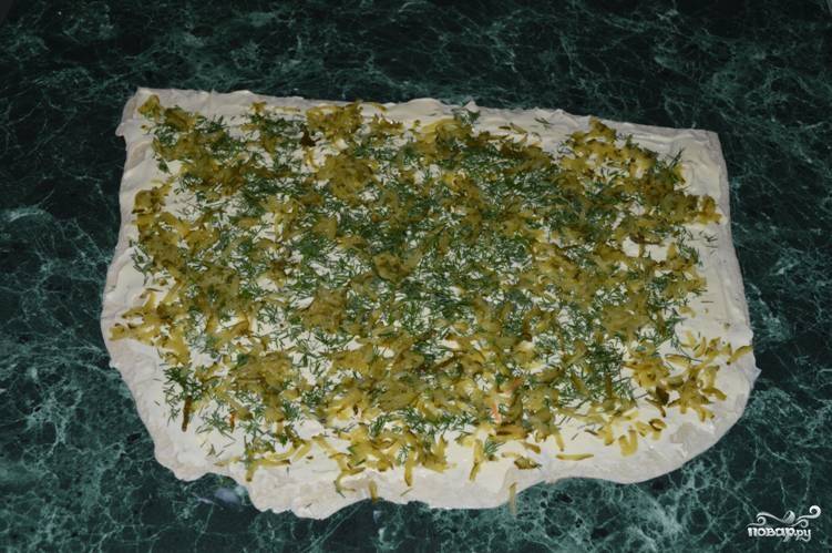 Возьмите первый лист лаваша, равномерно смажьте его плавленым сыром, посыпьте укропом и огурцами. 