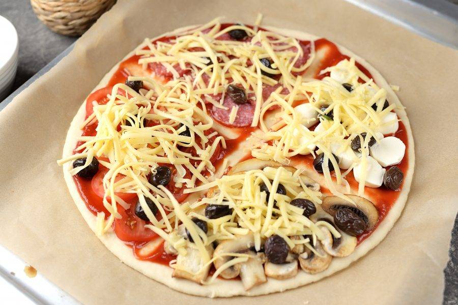 В последнюю очередь посыпьте всю пиццу натертым твердым сыром и отправьте в предварительно разогретую духовку на 10-12 минут при 200 градусах.