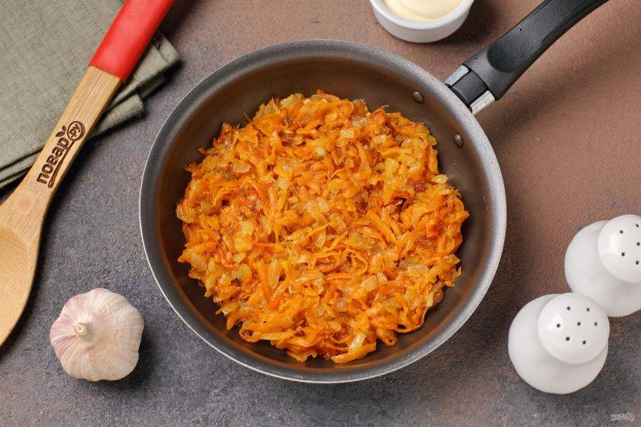 Лук нарежьте мелкими кубиками, морковь натрите на тёрке. Обжарьте овощи в сковороде до мягкости и переложите в глубокую тарелку.