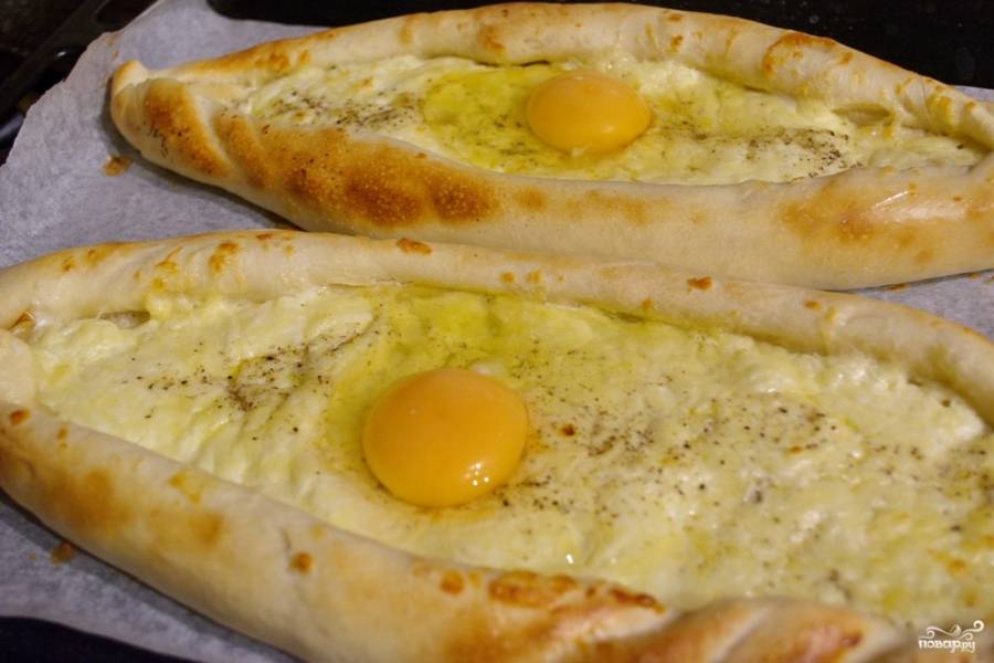 Достаньте противень из духовки. На каждый хачапури выложите сырое яйцо. Яйцо разбивать нужно аккуратно, чтоб не повредить желток. Верните противень в духовку. Запекайте еще 10 минут.
