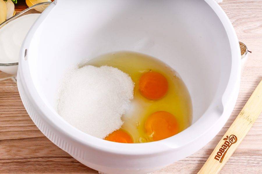 Куриные яйца вбейте в чашу кухонного комбайна или в высокую емкость миксера. Всыпьте сахарный песок и соль, взбейте все на самой высокой скорости техники примерно 4-5 минут в пышную массу.