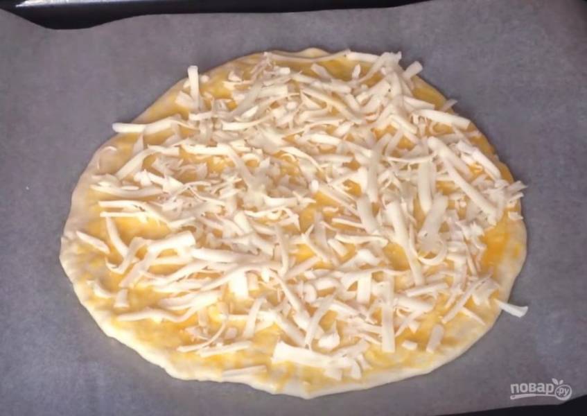 Перекладываем лепешку на противень, застеленный бумагой для выпечки. Сверху смазываем яичным желтком и посыпаем сыром. Выпекаем в разогретой до 200 градусов духовке в районе 15-20 минут.  