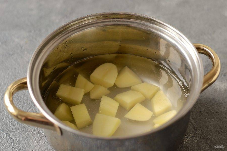 Картофель помойте, очистите от кожуры, нарежьте крупными ломтиками. Переложите в кастрюлю, залейте водой и поставьте вариться.