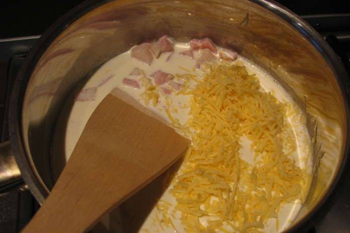 Добавляем в кастрюлю сливки, тертый сыр и порезанную мелкими ломтиками ветчину (не больше 60% от общего количества). Варим 10 минут, аккуратно помешивая.
