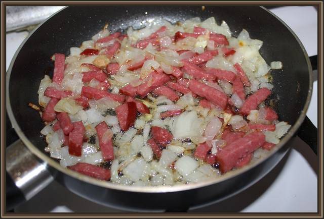Мелко нарежьте лук и колбасу. Лук обжарьте на растительном масле, до золотистой корочки. Затем добавьте колбасу, жарить 2-3 минуты, перемешивая.