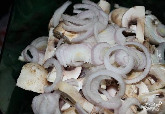 Отправьте грибы к мясу и очистите репчатый лучок. Нарежьте его на полукольца. Также переложите лук в миску к шампиньонам и мясу. 