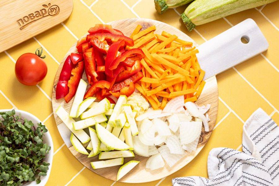 Морковь очистите и нарежьте соломкой, репчатый лук полукольцами, а болгарский перец с кабачком брусочками. Чеснок очистите и пропустите через пресс или натрите на мелкой терке.