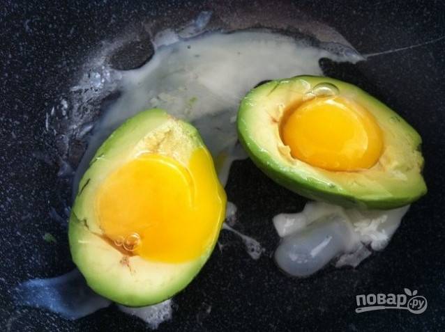 2. Разогрейте на сковороде масло. Выложите в него авокадо отверстиями вверх и разбейте в них по яйцу.