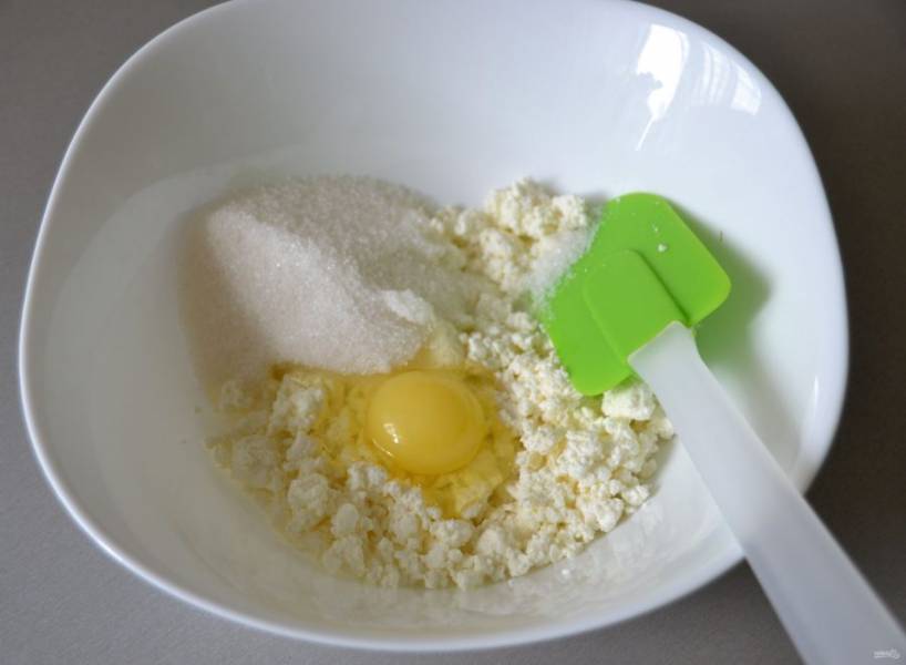 В миску выложите творог, вбейте яйцо, всыпьте сахарный песок.