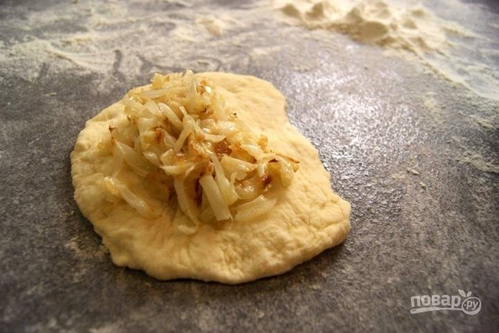 Достаем тесто, делим его на несколько частей. Каждую раскатываем в лепешку, в центр которой кладем начинку из капусты. 