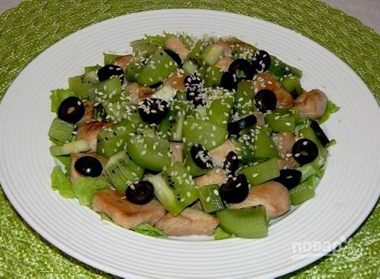 Выкладываем на салатные листья сначала кусочки курицы, а затем киви. Посыпаем маслинами и кунжутными семечками. Поливаем смесью оливкового масла и лимонного сока.
