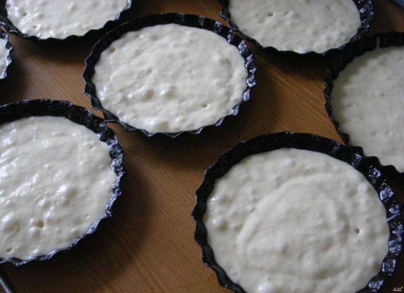 2.	Формочки для кексов смазываем подсолнечным маслом, затем разливаем в них полученное тесто. Сметану соединяем с сахаром и выкладываем слоем в 1-2 сантиметра сверху на тесто. 