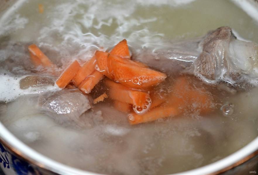В кастрюлю сложите мясо и морковь, очищенную и нарезанную крупными кусками. Залейте холодной водой, добавьте оливковое масло и оставьте вариться минут 30 на среднем огне, регулярно снимая пену.