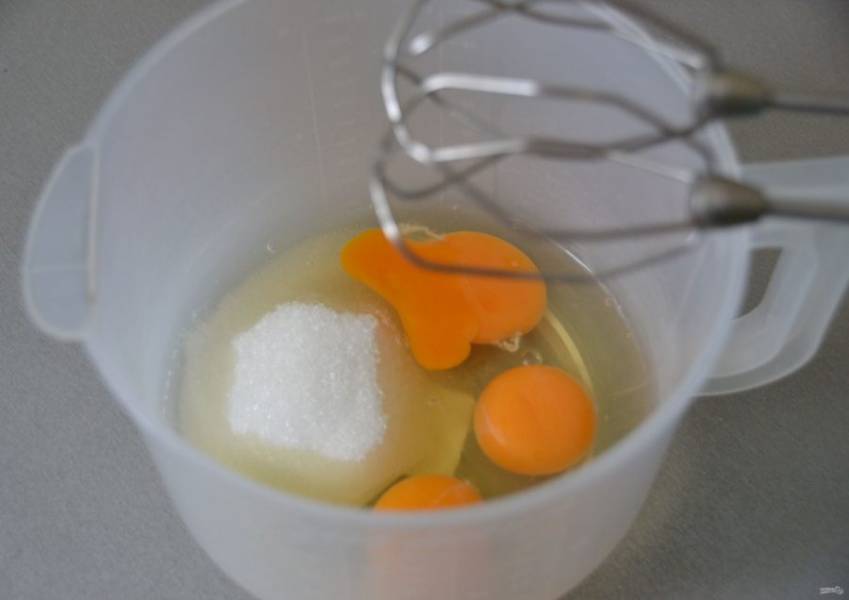 В емкость для взбиваний вбейте яйца, добавьте 80 грамм сахара, щепотку соли и взбейте в пышную пену.